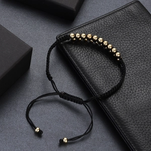 Detailed macro view of gold beads on black woven rope bracelet over leather texture