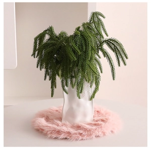 Detail of a round pink plush Christmas tree skirt with a white vase and green foliage
