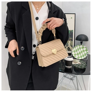 Chic beige quilted handbag with gold heart lock and pleated handle shown in a cafe setting