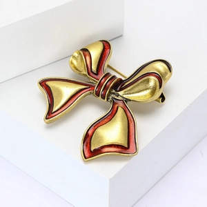 Elegant vintage gold-plated bow brooch with red enamel trim on white display stand