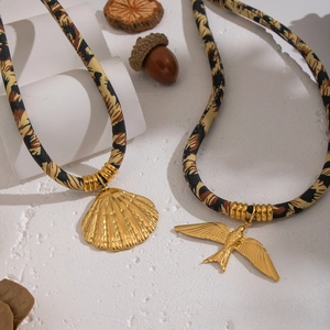 Leopard print silk scarf necklace with gold shell and bird pendants on white surface
