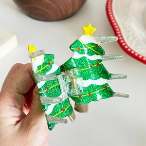 Sparkly green Christmas tree hair claw clip with red dots and yellow star held in hand