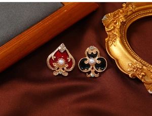 Macro shot of vintage enamel poker heart and club pins with pearls on silk backdrop