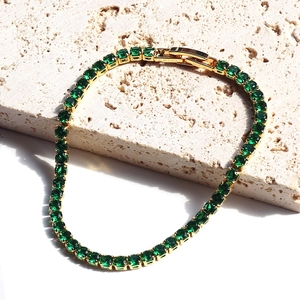 Elegant gold tennis bracelet with emerald green square zircons on rustic stone base