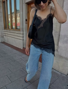 Détail d'un caraco noir en dentelle effet soie avec un jean bleu à jambes larges