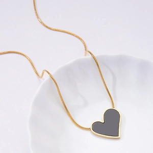 Detailed view of an asymmetric black heart pendant on a gold snake chain over a white plate