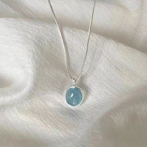 Macro shot of minimalist silver chain with an oval light blue gemstone pendant on fabric