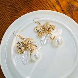 Detail of French vintage gold earrings with white petals, pearls, and sun face charms
