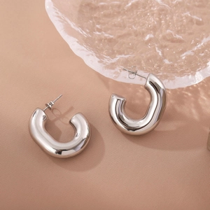 Polished silver stainless steel thick C-shaped hoop earrings on a textured glass plate