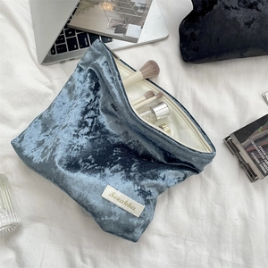 Detail of blue velvet makeup bag with zipper closure and brand label on white fabric