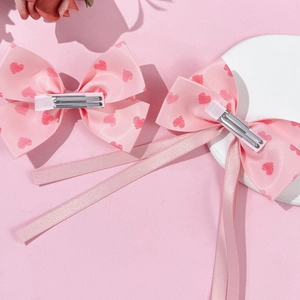 Pink bow hair clips with heart patterns and long ribbons on metal crocodile clips