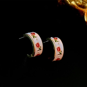Detail of C-shaped gold-plated earrings with white enamel and vintage red rose motifs