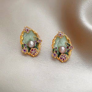 Detailed close-up of retro floral enamel earrings with pearls on champagne silk fabric
