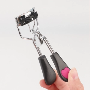 Stainless steel eyelash curler with comb and pink heart detail held in hand