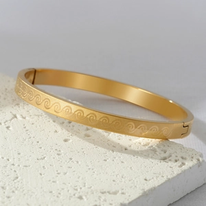 Minimalist gold titanium steel bangle with elegant etched wave pattern on white stone