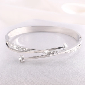 Close-up of silver-tone crisscross bangle with sparkling pave-set stones on white silk