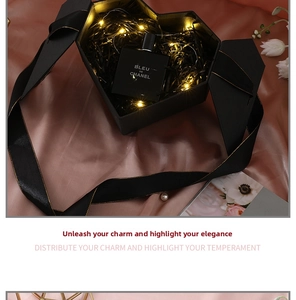 Close-up of heart-shaped black matte gift box with gold-edged ribbon and LED lights
