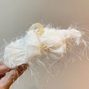 Vue détaillée d'une pince à cheveux en acrylique crème avec franges douces et pompons