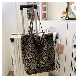 Leopard print canvas tote bag featuring a metal handmade label hanging on a suitcase handle