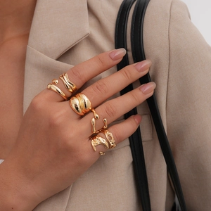 Dettaglio di anelli dorati stile lava geometrica indossati da una modella in abito beige