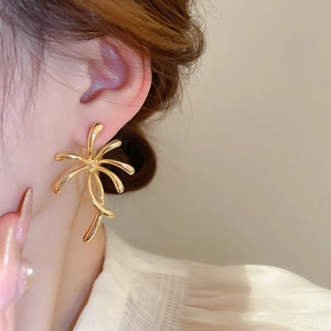 Close-up of gold plated abstract flower earrings worn by a model in warm light