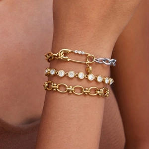 Detailed view of layered 18K gold clip chain bracelet with heart pendant and tennis link