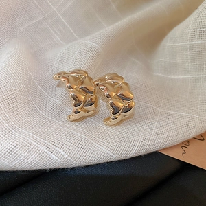 Detailed shot of interlocking gold heart stud earrings on elegant textured fabric