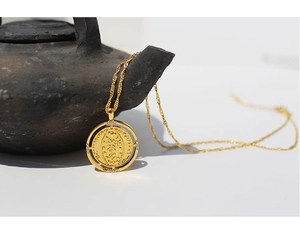Detailed view of vintage gold coin necklace with cubic zirconia on black teapot