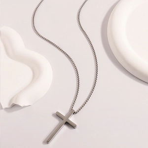 Detailed view of silver stainless steel cross necklace on geometric display stand