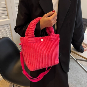 Bright pink corduroy bucket bag with white snap button and detachable strap handheld by model