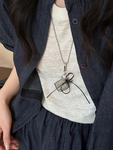 Close-up of a silver beaded necklace with a sparkling rhinestone cube and black bow knot