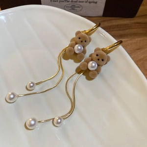 Close-up of flocking bear earrings with long gold tassels and white pearls on a shell tray