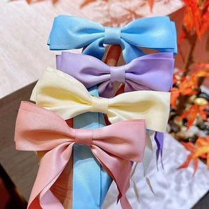 Detail of four colorful satin bow hair clips in blue, purple, cream, and pink shades