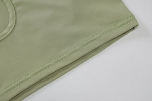 Detailed close-up of double-stitched hem on a green slim-fit knit crop top vest