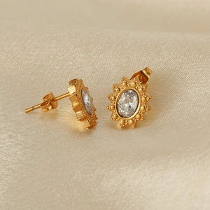 Detailed macro view of gold-plated stud earring with oval crystal on beige silk fabric