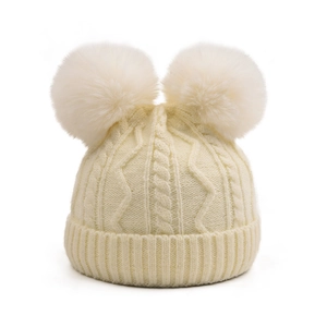 Detailed cable knit texture of cream winter hat with two large detachable faux fur pom-poms