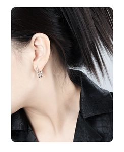 Close-up of a silver twisted geometric hoop earring worn on a female model's earlobe