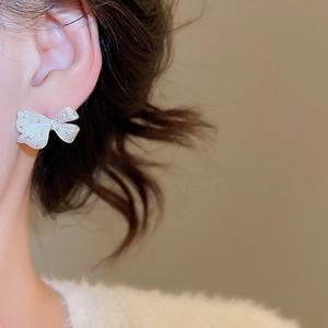 Macro close-up of a silver bow earring with brushed metal texture worn by a model