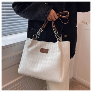 Detail of white quilted tote bag with brown leather and silver chain strap on model
