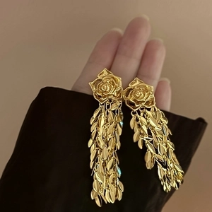 Détail de boucles d'oreilles élégantes en forme de rose dorée avec pampilles sur la main