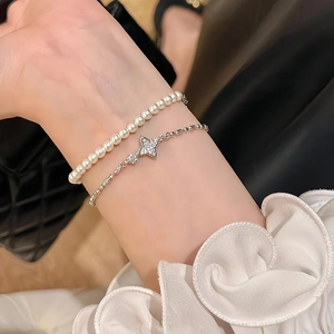 Close-up of stacked elegant pearl bracelet and silver star pendant chain on wrist