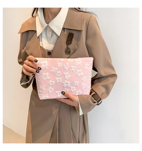 Pink embossed fabric clutch bag with white 3D floral textures held by a model in a trench coat