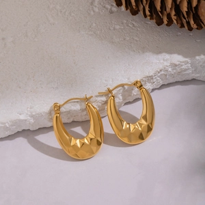 U-shaped geometric gold earrings with diamond-cut texture on a natural stone base