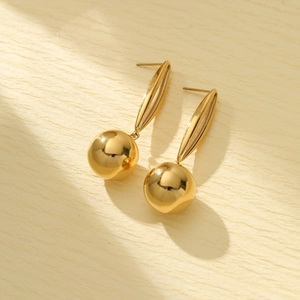Macro detail of high-shine gold-plated titanium ball drop earrings on beige paper
