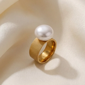 Macro view of a gold wide band stainless steel ring with a large white round pearl