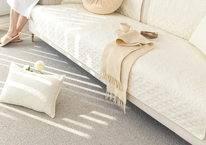 Close-up of cream quilted sofa cover with embossed floral pattern and scalloped edges
