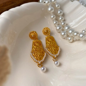 Detail of golden hollow floral earrings with vintage pearls on a decorative shell tray