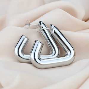 Modern silver triangular hoop earrings with polished metal finish on soft beige fabric