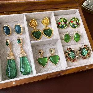 Close-up of vintage gold heart earrings with green gems in a wooden jewelry box