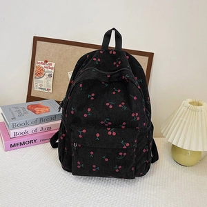 Detail of black corduroy backpack with red cherry pattern on textured tablecloth